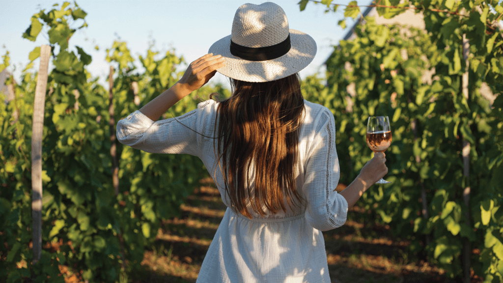 woman walking through vineyard with rose wine glass